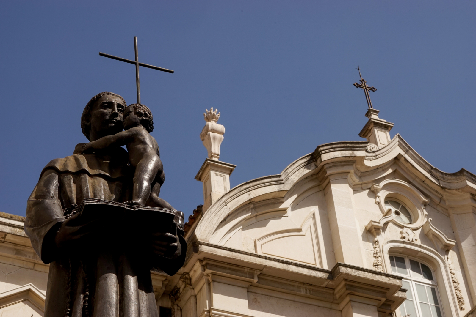 Uma estátua de um homem com uma criança ao colo, diante de uma igreja antiga